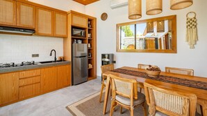Une cuisine moderne avec des meubles en bois, un réfrigérateur en acier inoxydable et un coin repas comprenant une table et des chaises en bois.