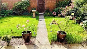 Un camí al jardí que condueix a una porta de fusta, envoltat de vegetació exuberant i plantes en testos.