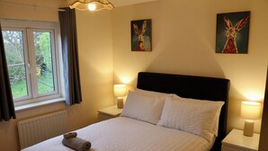 Una habitació d'hotel amb un llit, dues tauletes de nit, una finestra amb cortines i dos quadres penjats a la paret.