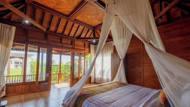 A wooden room with a bed, curtains, and a view of the outdoors. - One Bedroom Villa With Swimming Pool (Tegallalang)