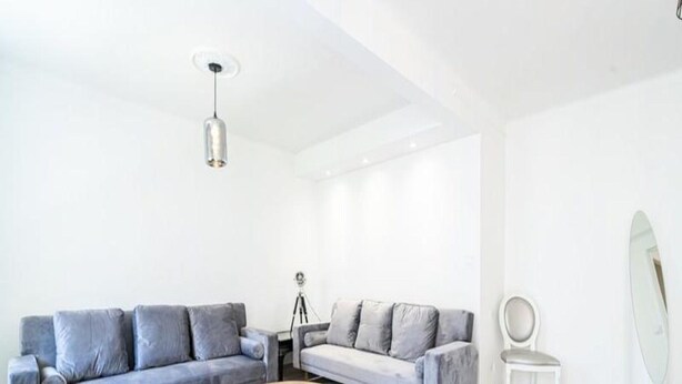 Ein modernes Wohnzimmer mit zwei grauen Sofas, einem runden Couchtisch, einem Stativ und einem weißen Sessel.
