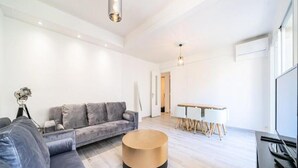 Ein modernes Wohnzimmer mit einem grauen Sofa, einem runden Couchtisch und einem Essbereich mit weißem Tisch und Stühlen.