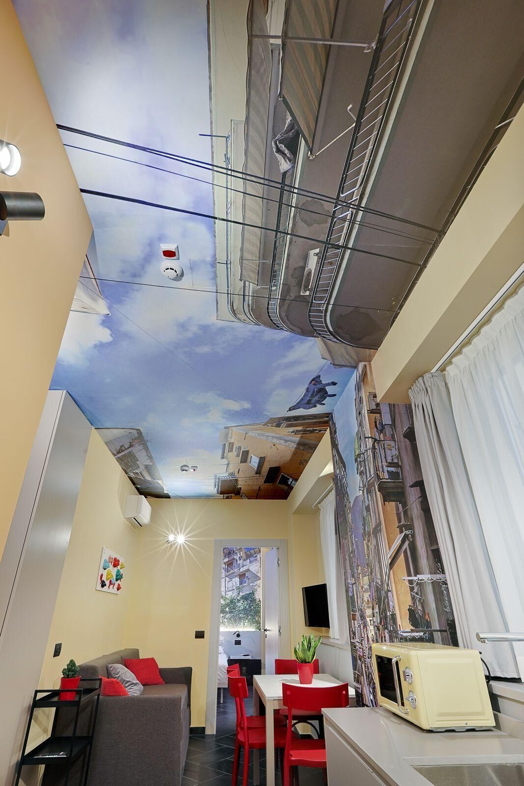 A room with a mural ceiling, a dining area with red chairs, a small table, and a vintage-style refrigerator.
