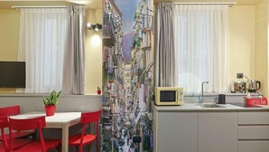 Een smalle gang met uitzicht op een drukke straat, een eetgedeelte met rode stoelen en een kitchenette met een koffiebar.
