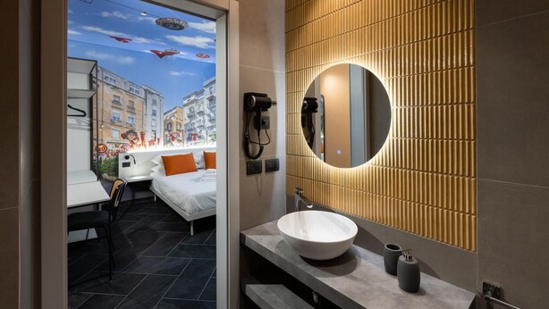 Een moderne badkamer met een grote spiegel, een witte wastafel en uitzicht op een stadsgezicht door een raam.