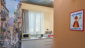 Een keuken met een raam, een magnetron, een koffiehoek en een muur met een poster.
