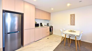 A modern kitchen with a stainless steel refrigerator, light wood cabinets, a microwave, and a dining area with a white table and chairs. - Modern Manchester St Stay - 1BR with Balcony (Christchurch)