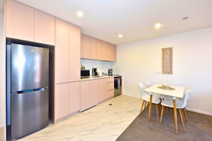 A modern kitchen with a stainless steel refrigerator, light wood cabinets, a microwave, and a dining area with a white table and chairs. - Modern Manchester St Stay - 1BR with Balcony (Christchurch)
