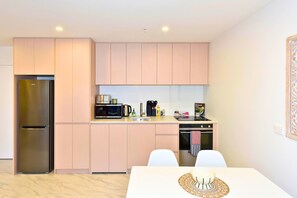 Eine kompakte Küche mit Kühlschrank, Mikrowelle, Backofen und einem Essbereich mit Tisch und Stühlen.