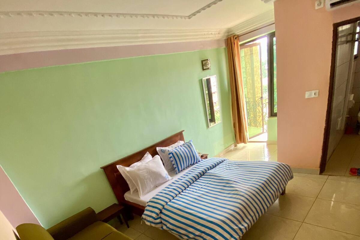 A hotel room with a bed, a sofa, a mirror, and a door leading to a balcony.