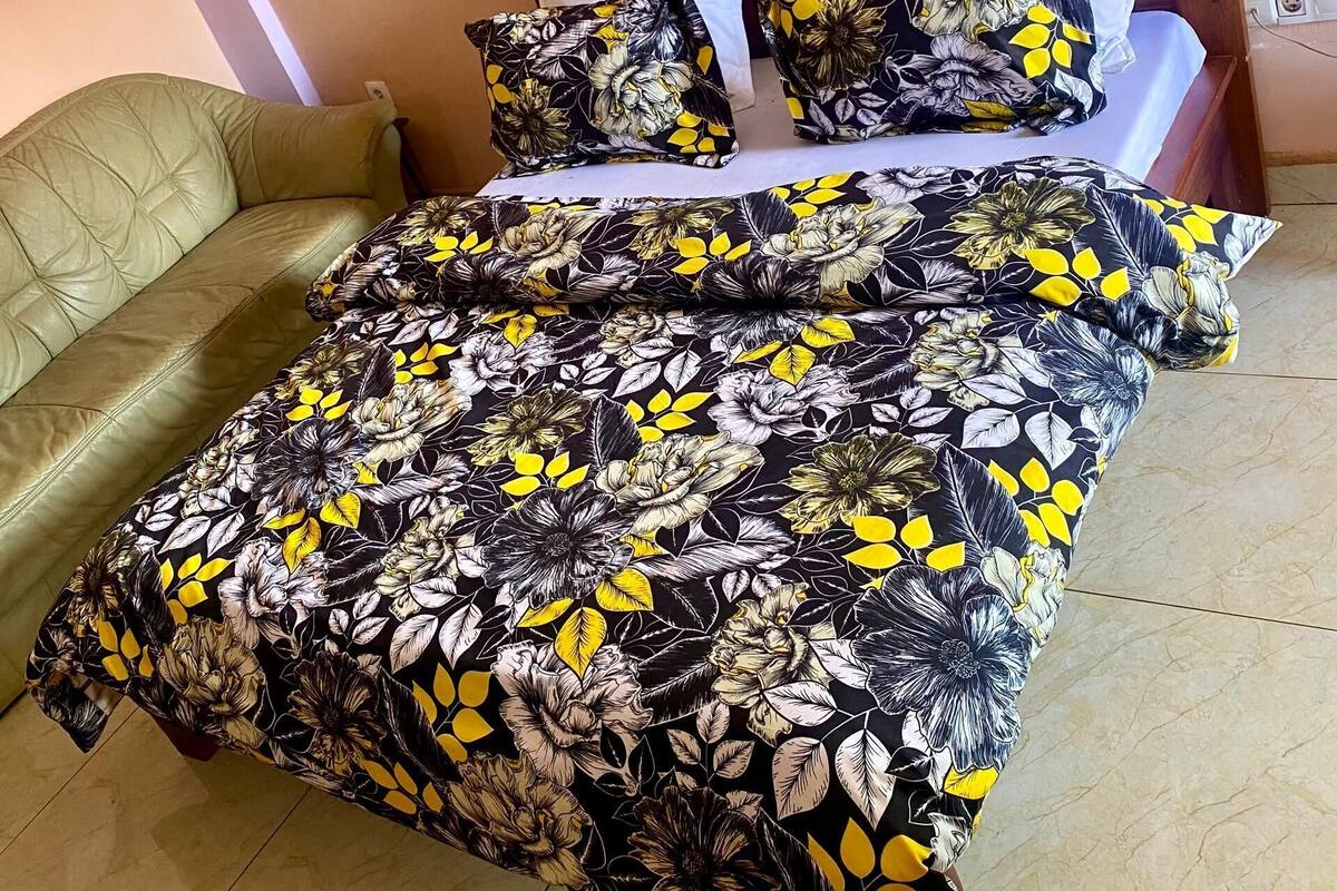A bed with a floral bedspread, a wooden headboard, and a green armchair.