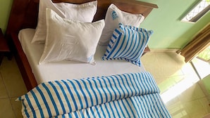 A bed with white and blue striped bedding, a wooden headboard, and a window with bars. - BALATSIT HOTEL HOTEL (Bafoussam)