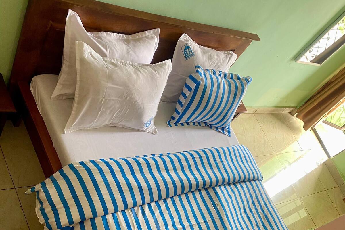 A bed with white and blue striped bedding, a wooden headboard, and a window with bars.