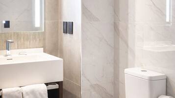 A modern bathroom with a marble wall, a white sink, a toilet, and a mirror.