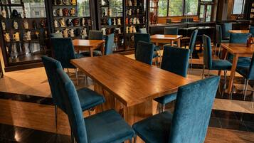 Un restaurant avec des tables en bois et des chaises bleues, une étagère où sont exposées des tasses en céramique, et de grandes fenêtres.