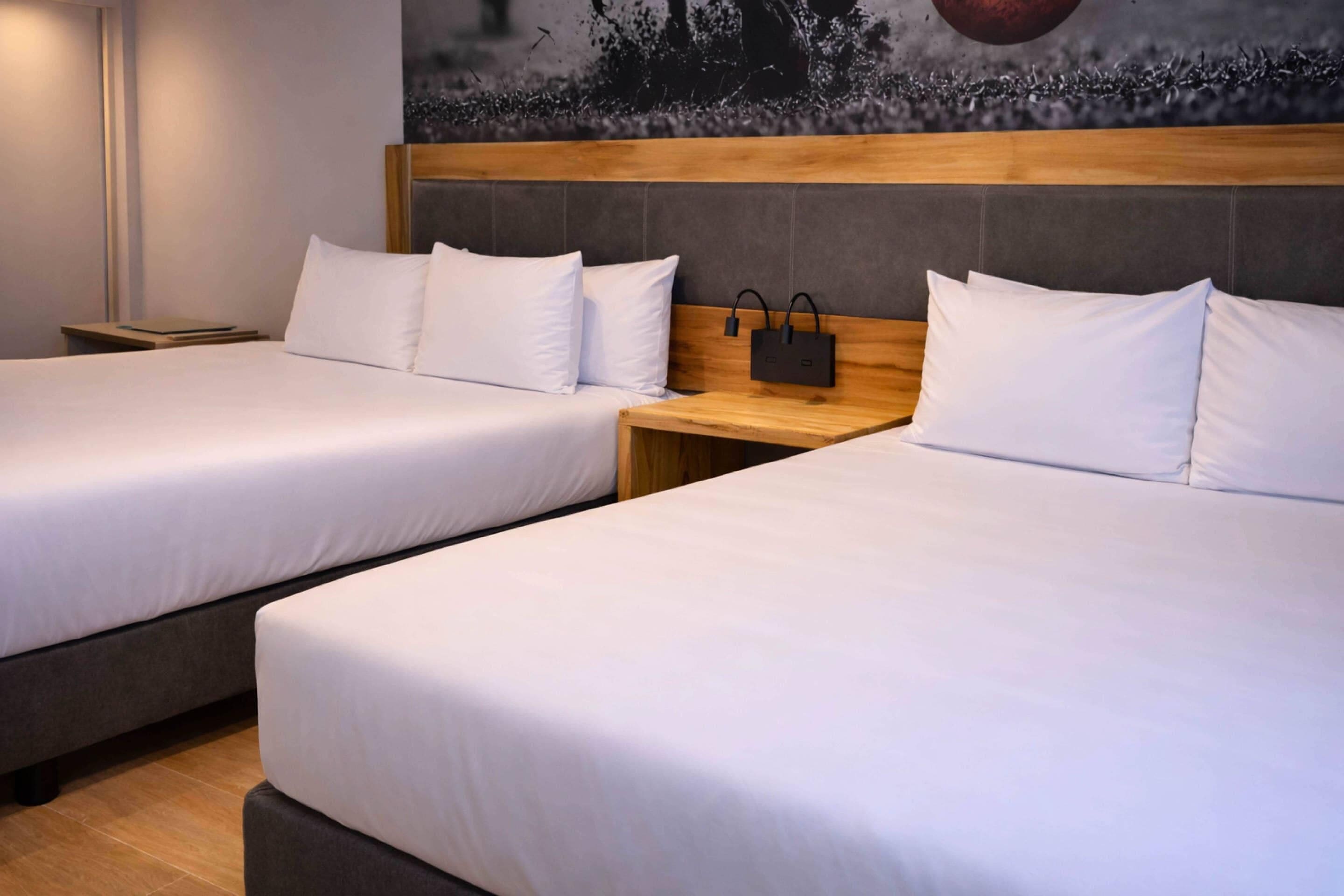 Dos camas individuales con cabeceras de madera, ropa de cama blanca y una mesita de noche con toma de corriente.