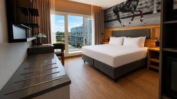 Ein Hotelzimmer mit einem großen Bett, einem Schreibtisch, einem Fernseher und Blick ins Freie.