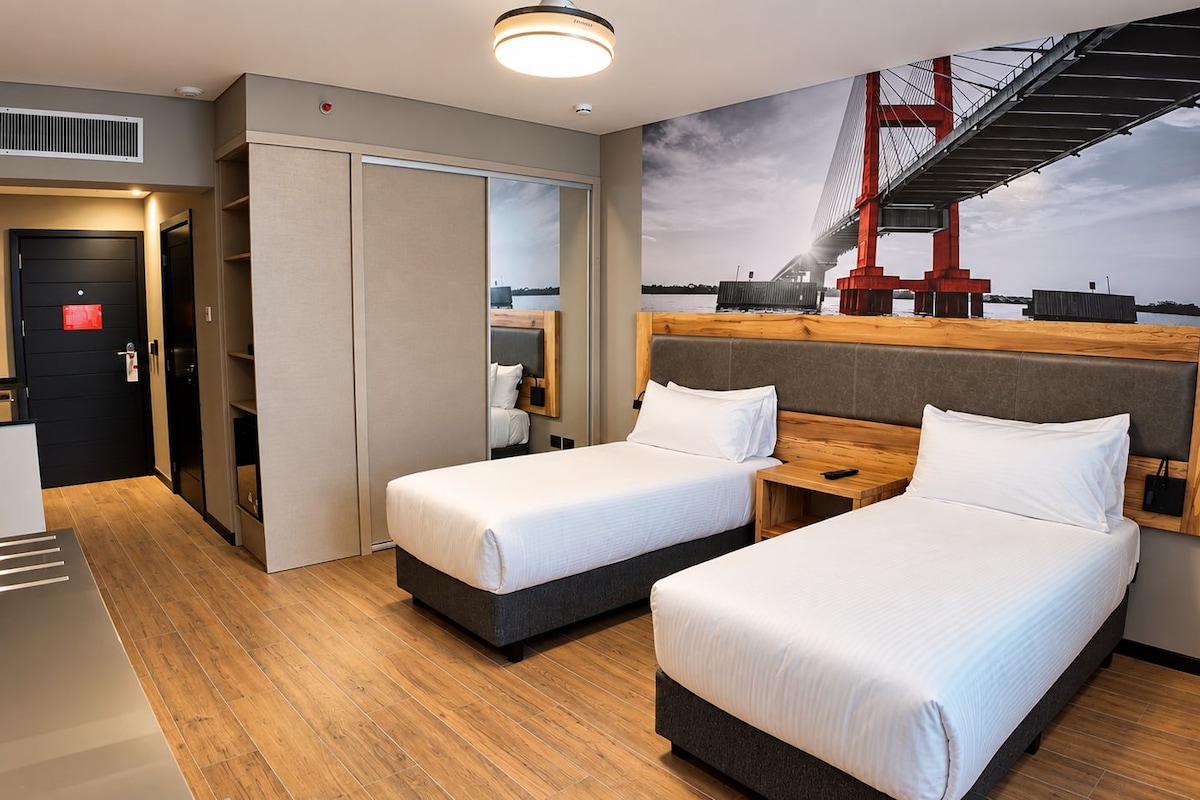 Habitación de hotel con dos camas, un ventanal con vistas a un puente y un diseño moderno.