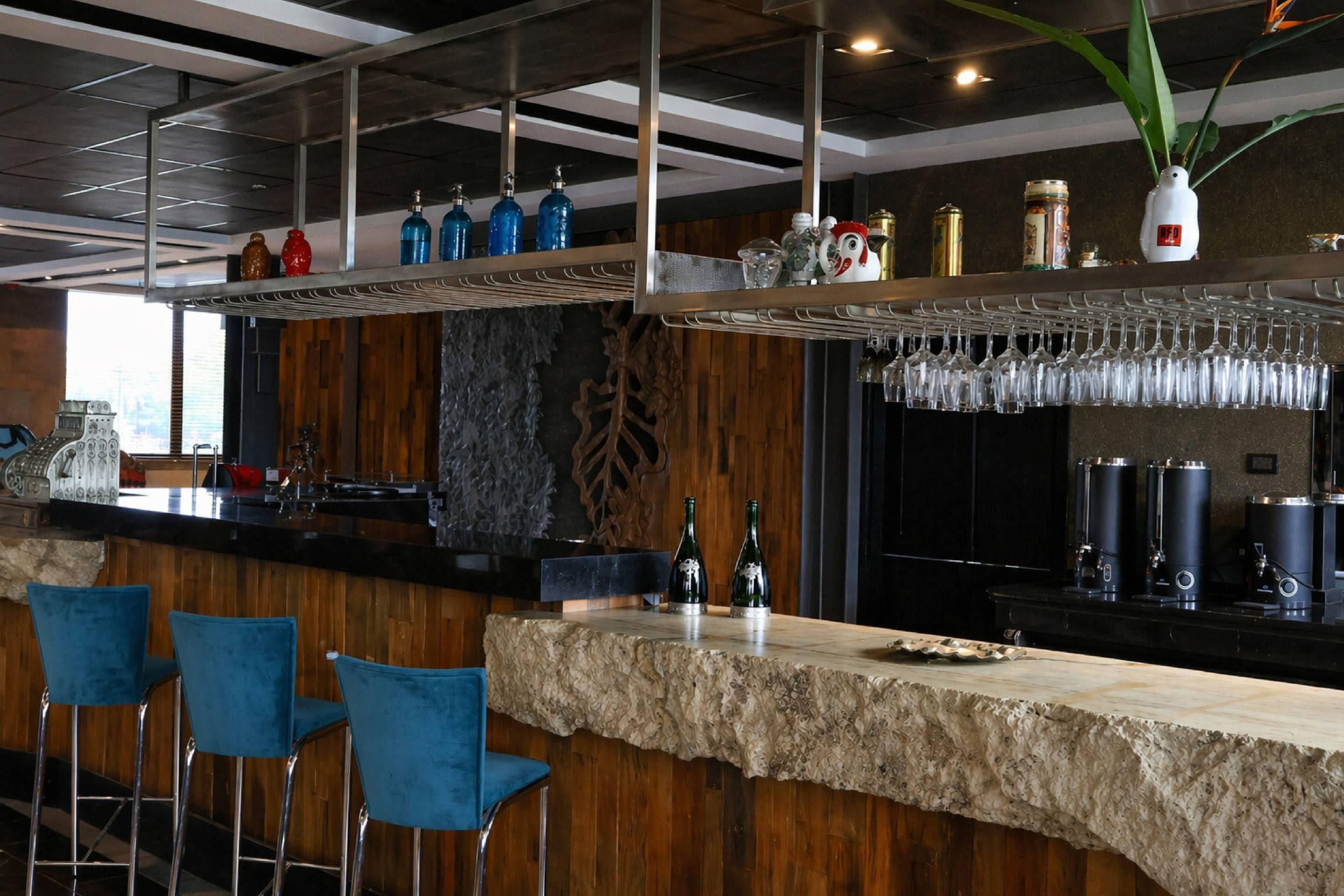 A bar area with a stone countertop, blue bar stools, and a variety of bottles and glasses on shelves.