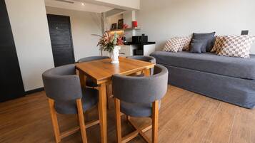 Un espace de vie moderne comprenant une table à manger, quatre chaises grises, un canapé gris et un coin cuisine à l’arrière-plan.