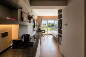 A modern kitchen with a built-in coffee machine, a dining area with a table and chairs, and a large window with a view of greenery.