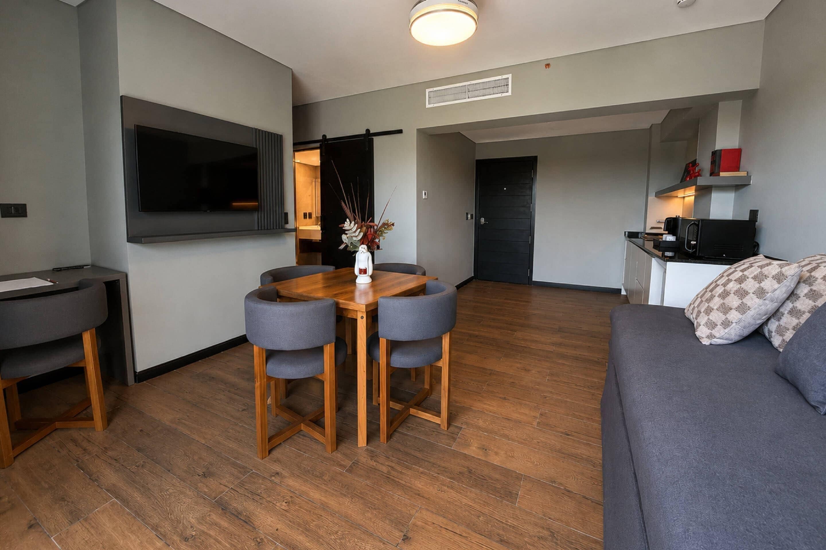 Een moderne woonkamer met een flatscreen televisie, een eettafel met stoelen, een bank en een keukenhoek met een magnetron.
