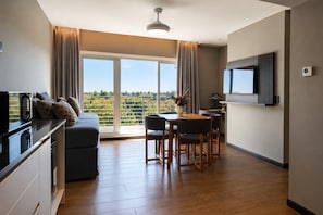 A modern living room with a sofa, dining table, chairs, a TV, and a large window with a view.