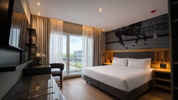 Habitación de hotel moderna con una cama grande, un escritorio, una silla, un televisor y vistas a la ciudad.