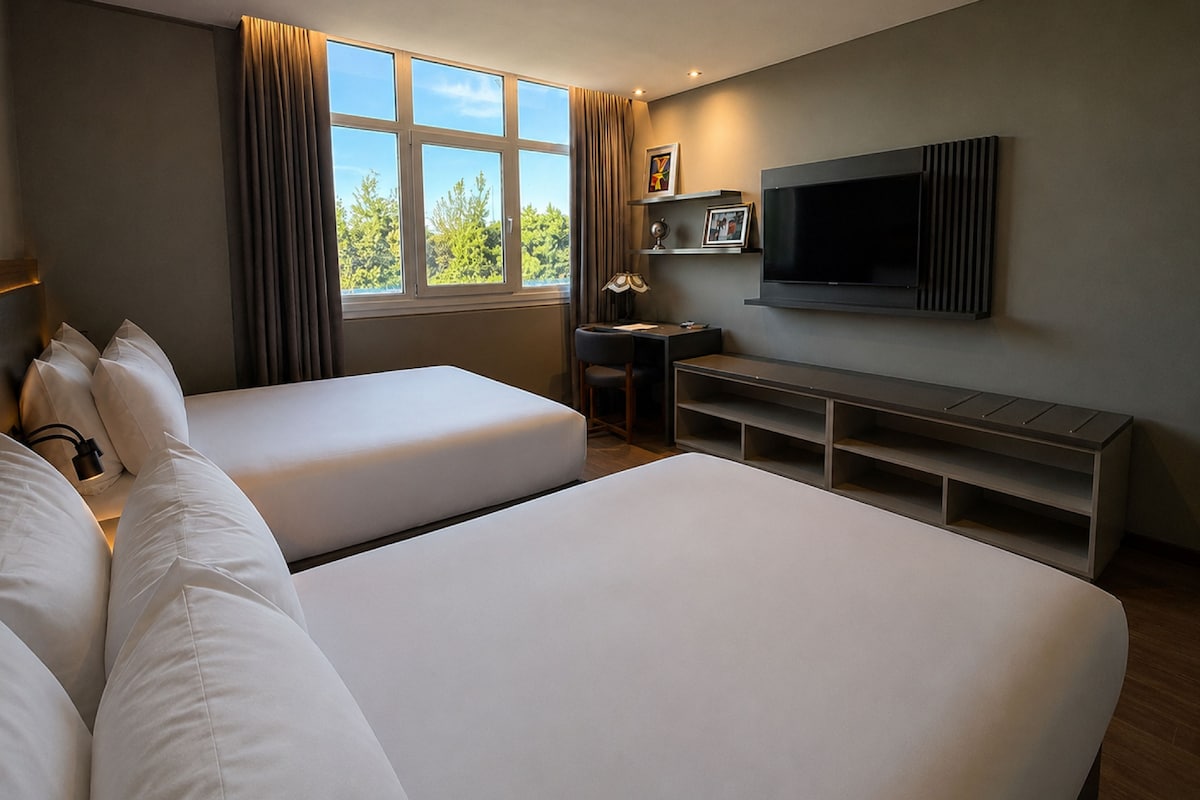 Habitación de hotel con dos camas, un escritorio, una silla, un televisor y una ventana con cortinas.