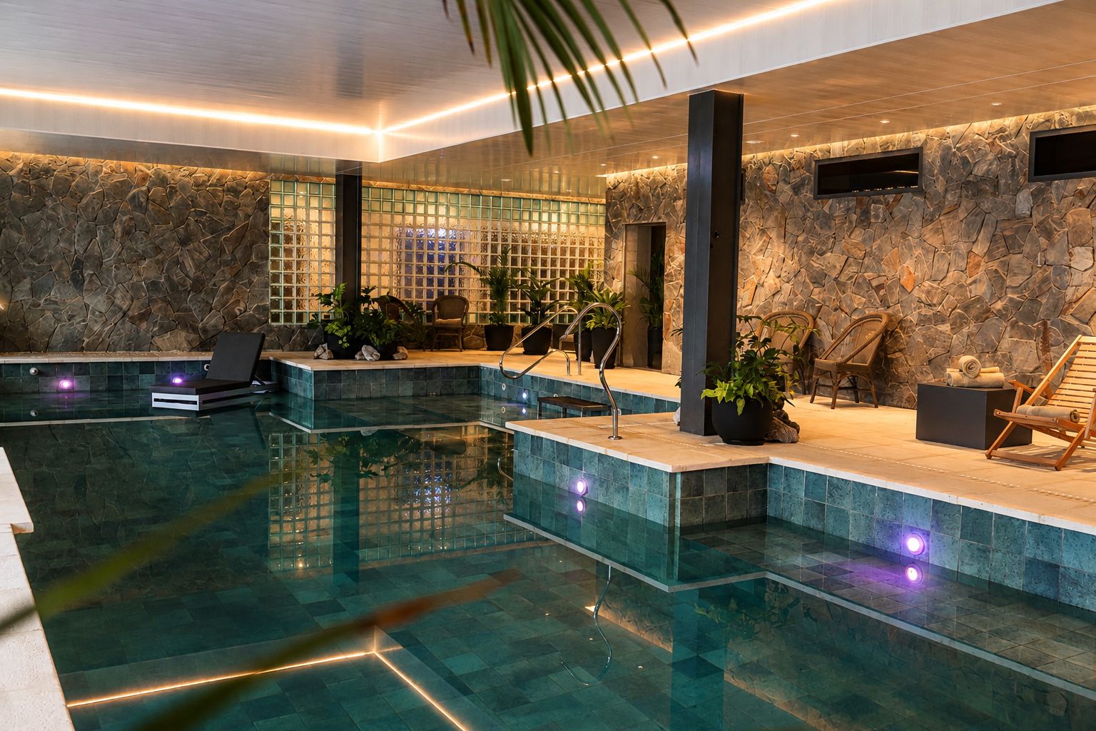 Una piscina interior moderna con agua cristalina, paredes de piedra y sillones de descanso.