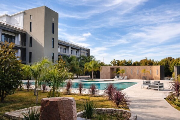 A modern building with a swimming pool, outdoor seating, and landscaped garden.