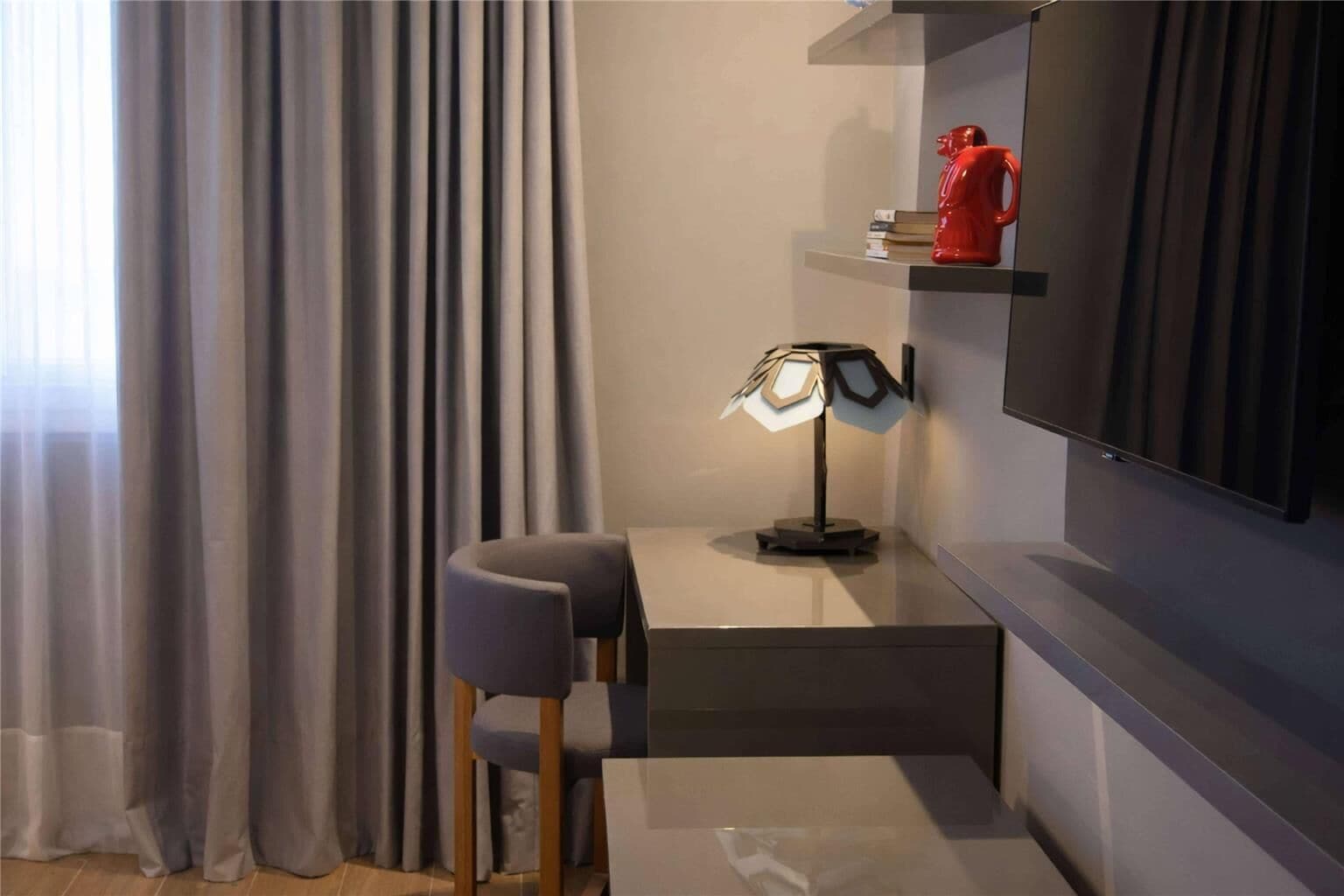 Una habitación moderna con escritorio, silla, lámpara y televisor montado.