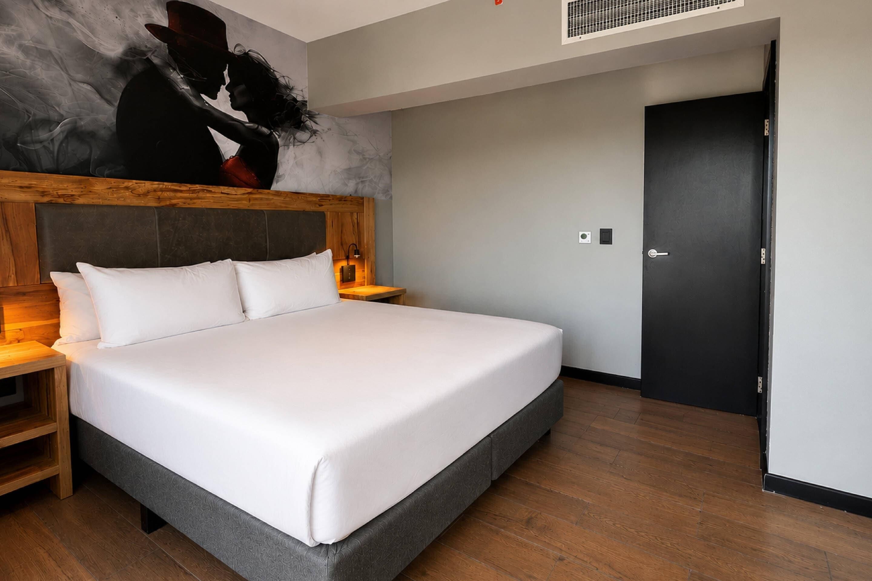 Ein modernes Hotelzimmer mit einem großen Bett, einem Holzkopfstück, Nachttischlampen und einer dunklen Tür.