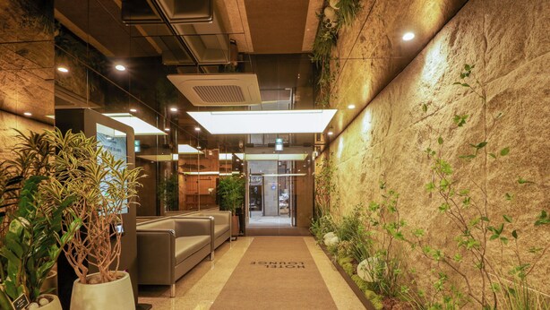 Un hall d’hôtel comprenant un comptoir d’accueil, un espace salon et un couloir recouvert de moquette.