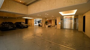 Un vaste espace de stationnement intérieur pouvant accueillir de nombreux véhicules, un ascenseur central et un mur en marbre.
