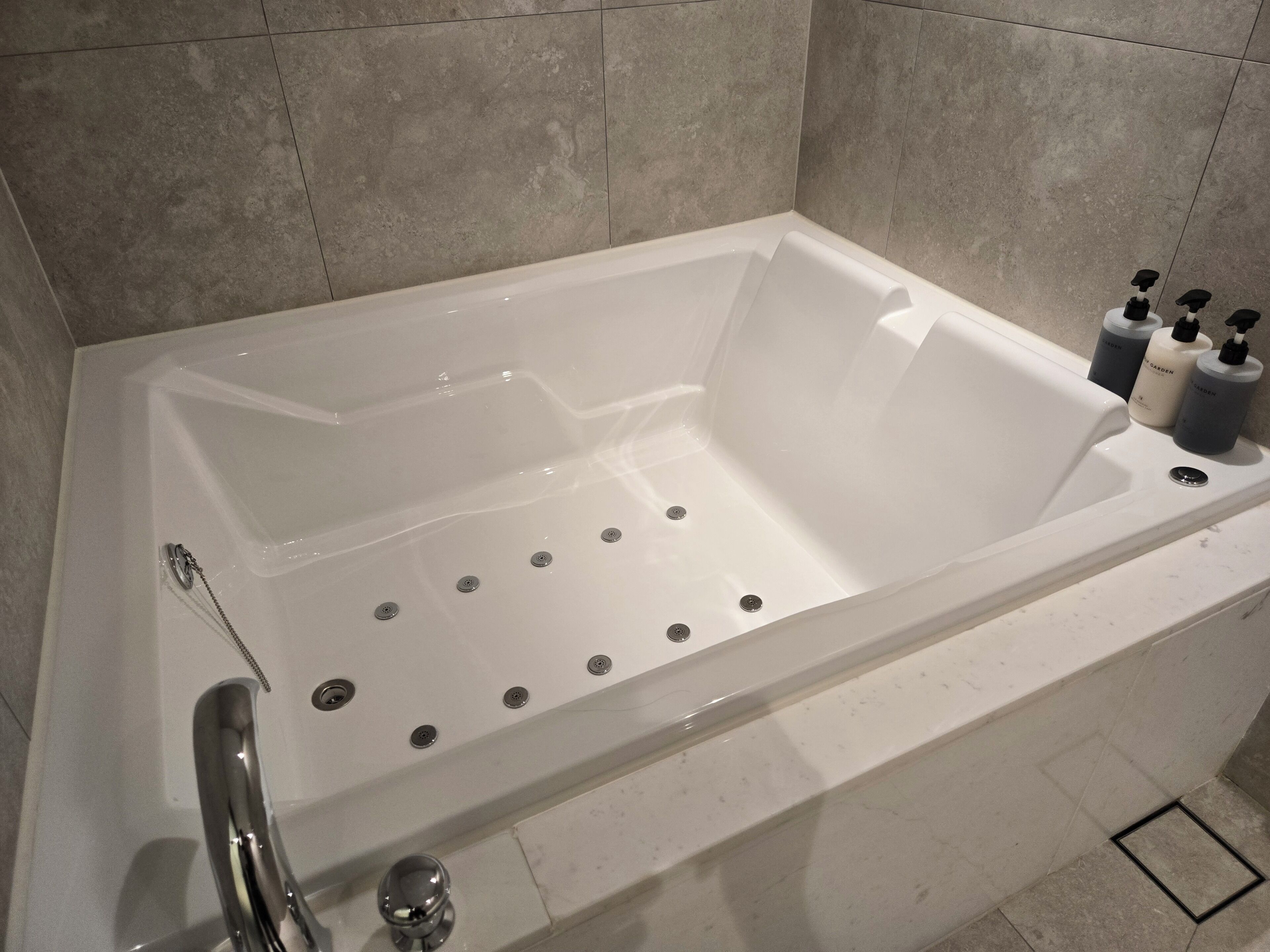 A modern bathroom with a large bathtub, multiple faucets, and toiletries on the side.