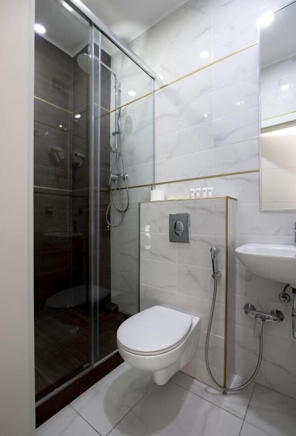 Ein modernes Badezimmer mit einer gläsernen Duschkabine, einer weißen Toilette und einem Waschbecken mit Spiegel darüber.