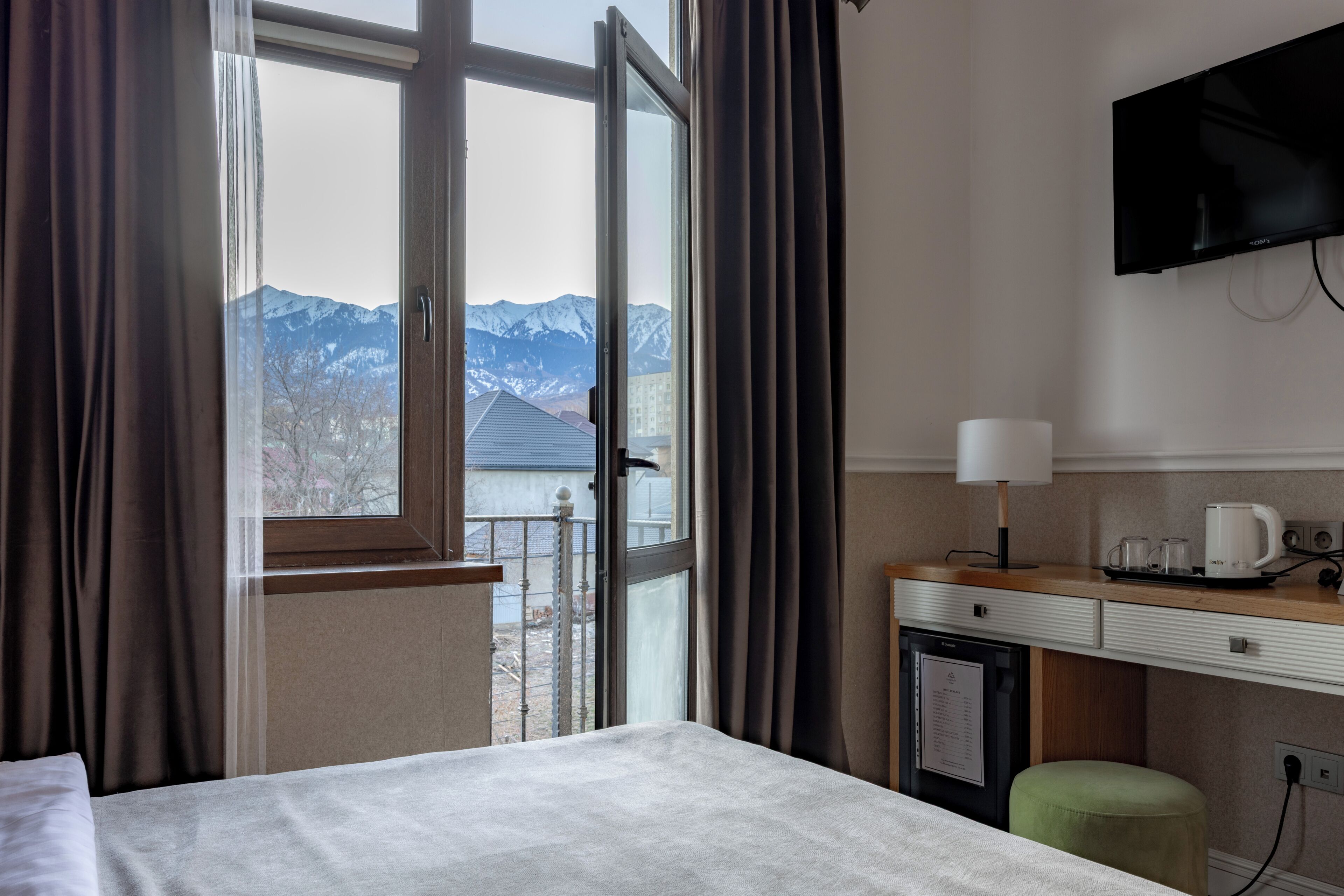 Una habitación de hotel con cama, escritorio, televisor y vista a las montañas.
