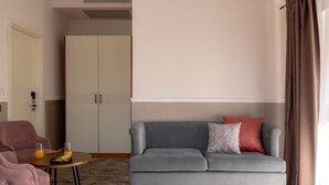 A modern hotel room with a grey sofa, a small round table with orange juice, a pink armchair, and a wardrobe. - Mountain View Boutique Almaty (Almaty)