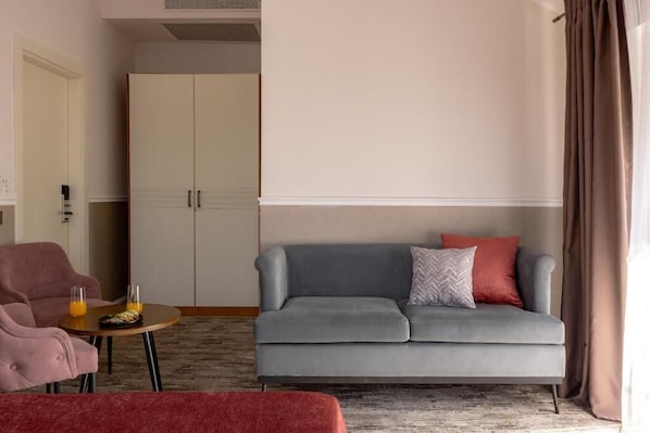 A modern hotel room with a grey sofa, a small round table with orange juice, a pink armchair, and a wardrobe. - Mountain View Boutique Almaty (Almaty)