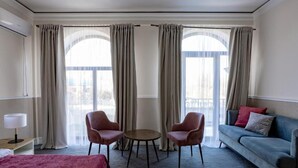 A hotel room with a bed, a round table, two chairs, a sofa, and large windows with curtains. - Mountain View Boutique Almaty (Almaty)