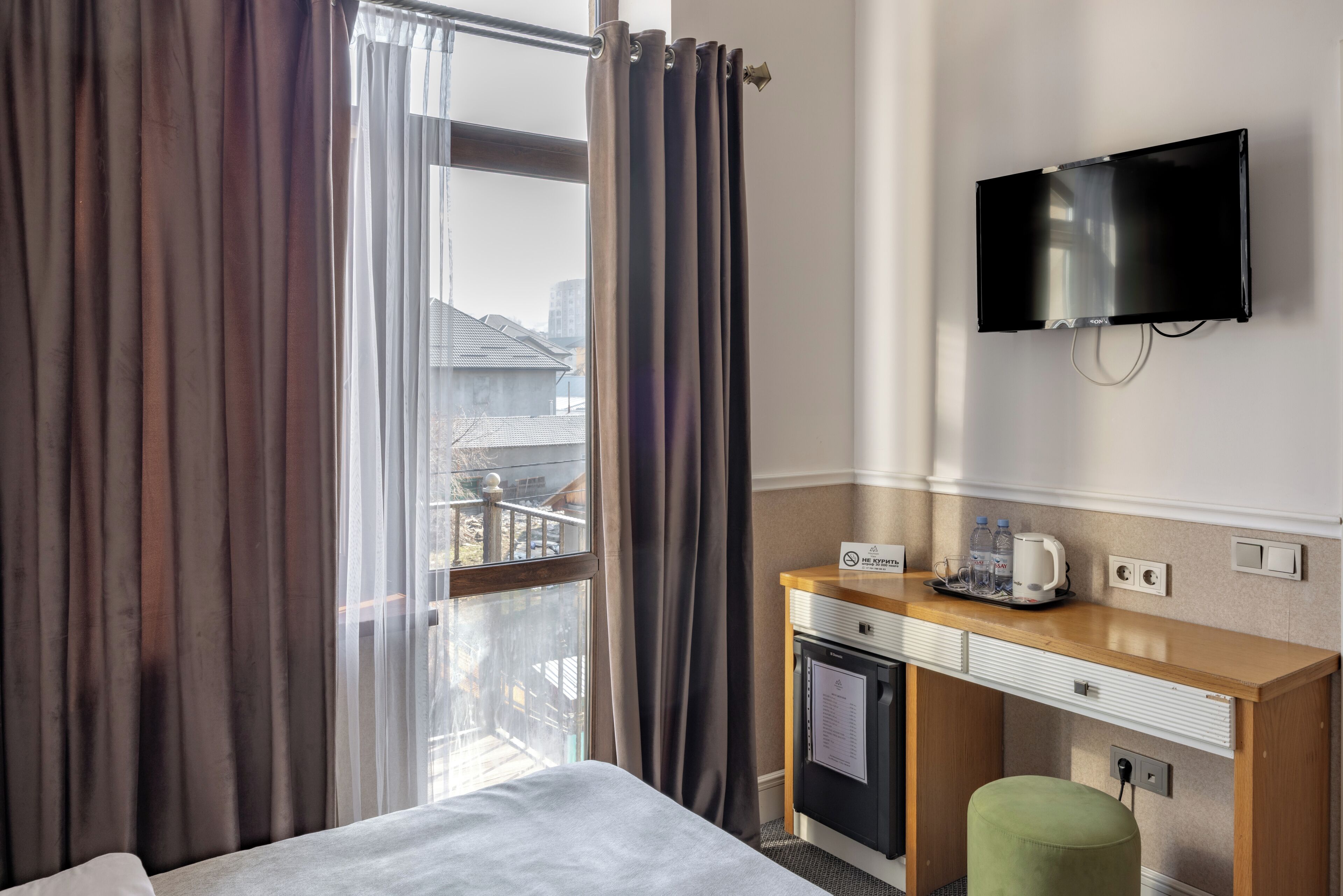 A hotel room with a bed, a desk with a television, a coffee maker, and a view of the city through the window.