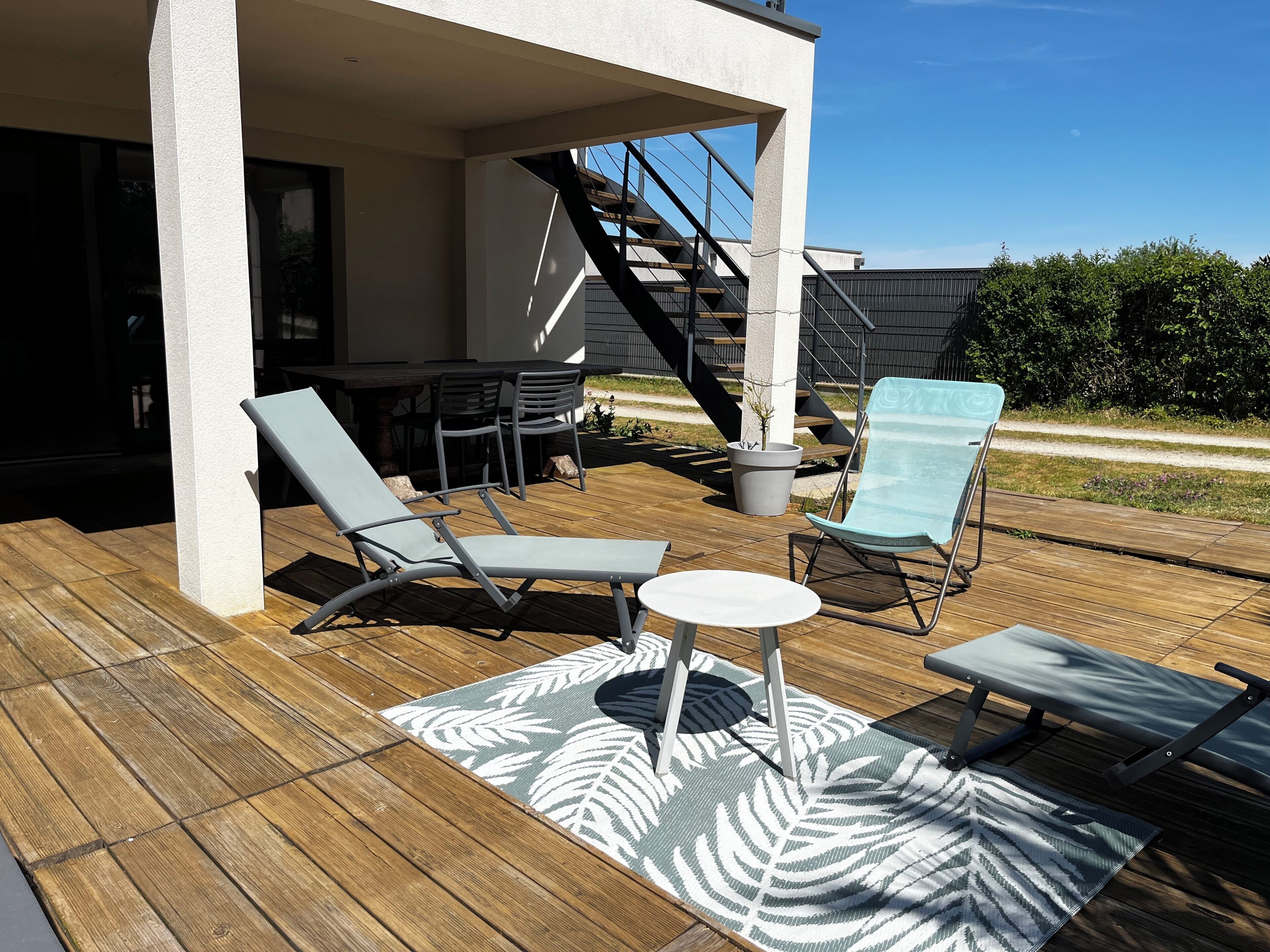 Un patio al aire libre con sillones de descanso, una mesa y una escalera que conduce a un nivel superior.
