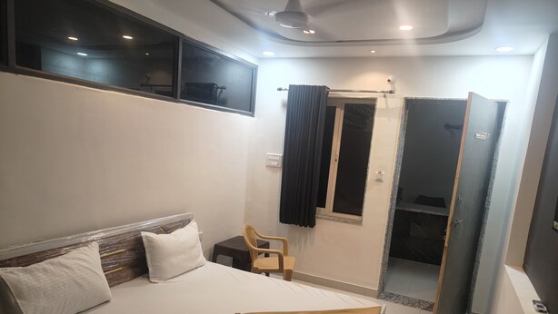 A bedroom with a bed, a chair, a window, and a bathroom door. - Hotel Maruti Inn (Sumerpur)