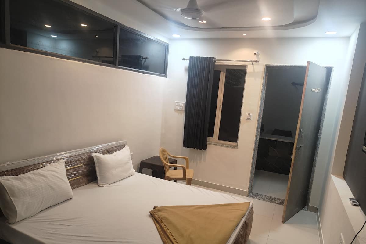 A bedroom with a bed, a chair, a window, and a bathroom door.