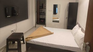 A hotel room with a bed, a small stool, a TV mounted on the wall, and an air conditioning unit. - Hotel Maruti Inn (Sumerpur)