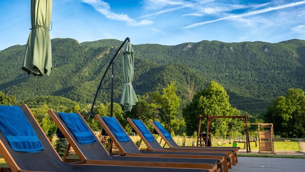 A row of wooden lounge chairs with blue towels, set against a backdrop of lush green mountains and a clear sky. - Villa Brusiana With Covered Heated Pool (Gospic)