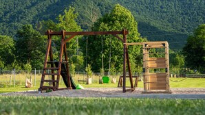 A playground with a swing set and a climbing structure in a park with a forested hill in the background. - Villa Brusiana With Covered Heated Pool (Gospic)