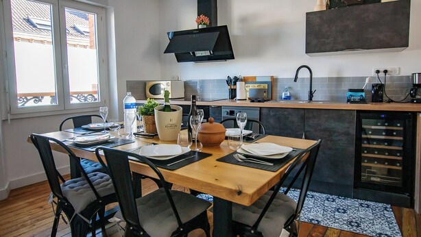 A modern kitchen with a dining area, featuring a wooden table, black chairs, and a built-in oven. - THE CHARM OF LES BERCEAUX: 5 minutes from Avenue de Champagne and right in the heart of the city (Épernay)