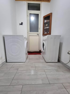 Una sala de bugaderia amb dues rentadores, un armari i una porta amb panell de vidre acidulat.